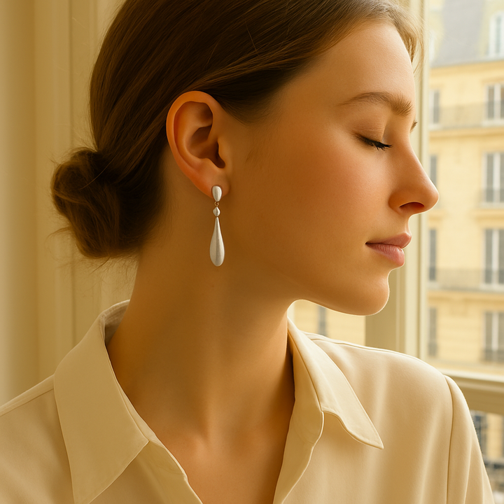 Mannequin de profil portant les boucles Célia, reflet lumineux sur l’argent, décor naturel chic.