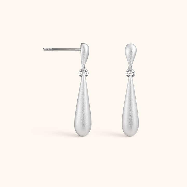 Boucles d’oreilles géométriques en argent posées sur tissu clair, ambiance lumineuse et élégante.